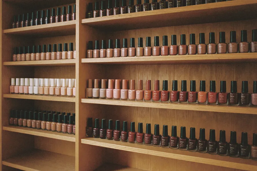 A floor-to-ceiling shelf of lacquer bottles graded bone to oxblood